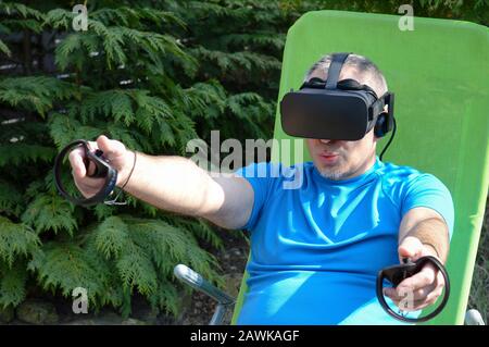 joyful mature man with virtual reality headset enjoy a game and experience the computer-generated simulation in his garden on a summer day Stock Photo