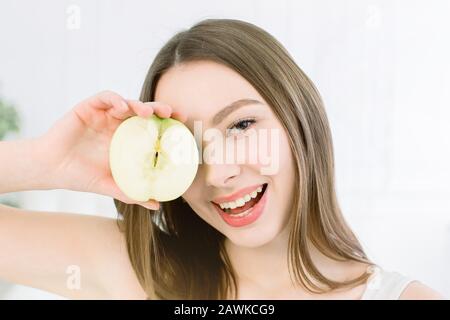 Smiling beauty woman holding half of green apple. The girl closes one eye with half an apple. Stock Photo