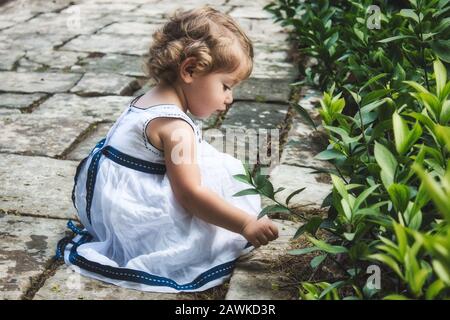 A beautiful cute young girl playing on a garden path with green leaf foliage Stock Photo