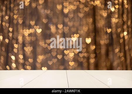 Empty white wooden tabletop on a gold blurred background with bokeh hearts. Image for montage or display your products. Copy space. Stock Photo