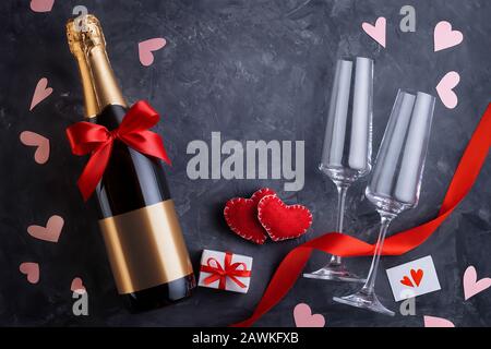 Top view of a bottle of champagne with a bow, two elegant glasses, two handmade hearts, a greeting card, a gift box, a red ribbon and scattered hearts Stock Photo