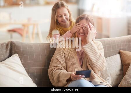 Warm toned portrait of cute girl playing peek a boo with mom while surprising her on Mothers day, copy space Stock Photo