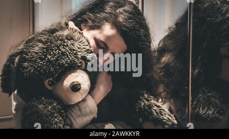 Woman hugging a teddy bear at home, looking sad and thoghtful. Stock Photo