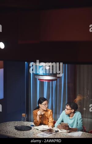 High angle portrait of two ethnic business people discussing project while working late in dark office, copy space Stock Photo