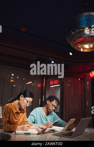 Vertical portrait of Asian businesswoman working late in dark office with African colleague, copy space Stock Photo