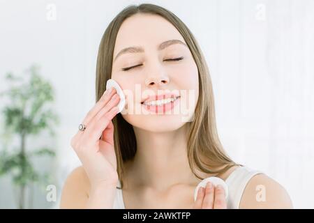 Portrait of pretty young woman using cotton pad over light background. Perfect Fresh Skin. Pure Beauty Model. Youth and Skin Care Concept, beauty Stock Photo