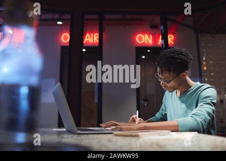 Side view portrait of young African-American man working late at home or in dark office, copy space Stock Photo