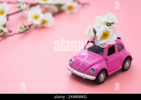 Corby, U.K. February 7, 2020. Miniature pink toy car with spring, summer flowers, on pink background. Minimal concept. Copy space.