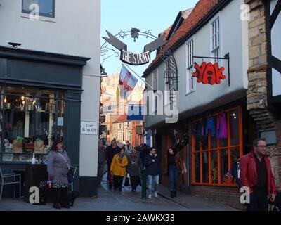 Shoppers at the entrance archway to The Strait in Lincoln, a narrow street full of independent shops and restaurants which leads up to the Cathedral Stock Photo