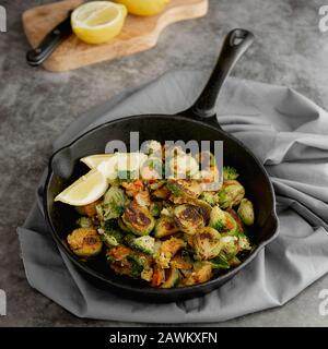 Roasted brussels sprouts in iron pan, with lemon slices. Dark background. Square image. Healthy food concept. Stock Photo