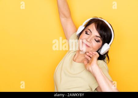 Beautiful Senior woman dancing and relaxing in the wireless headphones over yellow background Stock Photo