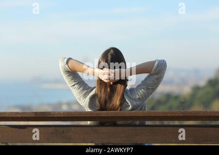 Back view of a woman resing sitting on a bench contemplating views in a city outskirts