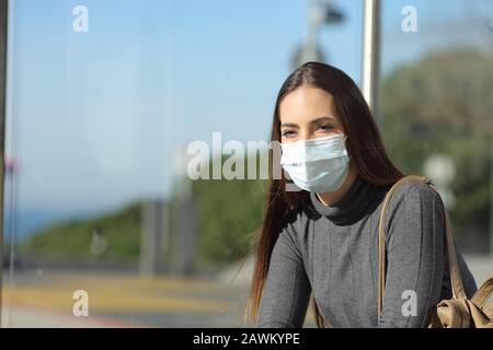 Worried woman with a mask preventing contagion waiting in a bus stop Stock Photo