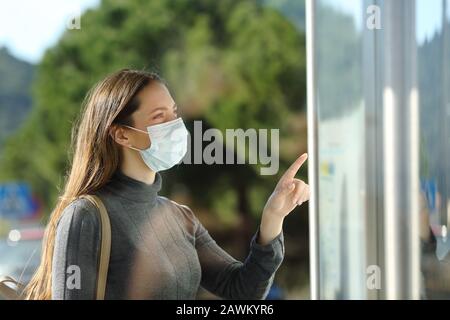 Casual woman wearing a protective mask checking schedule standing in a bus stop Stock Photo