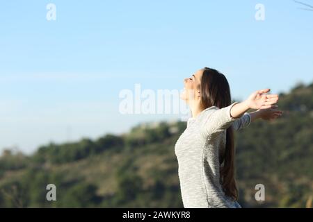 Side view portrait of a happy woman stretching arms breathing fresh air in the mountain Stock Photo