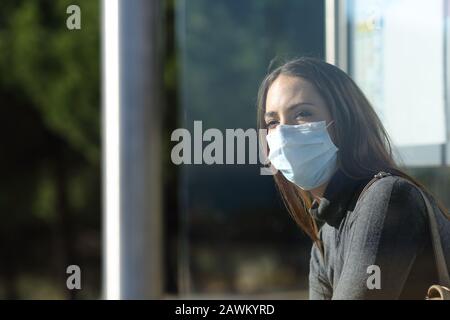 Woman wearing a protective mask to prevent virus contagion waiting in a bus stop Stock Photo