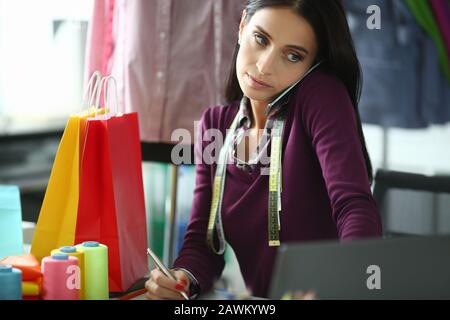 Tailor talking on phone with client in workshop. Stock Photo