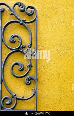 A Decorative Piece of Wrought Iron Mounted to a Bright Colored Stucco Wall Stock Photo