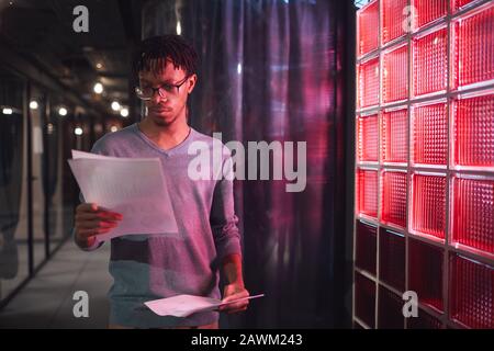 Waist up portrait of contemporary African man reading documents while standing outdoors in dim red lighting, copy space Stock Photo