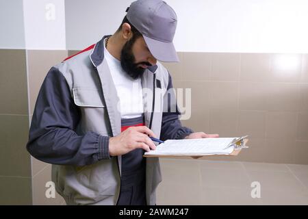 Concentrated young technician wearing overall standing and taking some notes Stock Photo