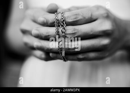 Black and white of woman hands praying holding a beads rosary with Jesus Christ in the cross or Crucifix on black background. Stock Photo