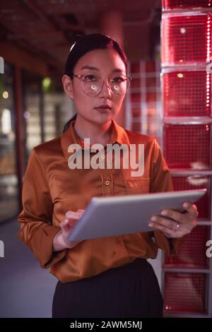 Waist up portrait of contemporary Asian businesswoman looking at camera while posing in futuristic office interior Stock Photo