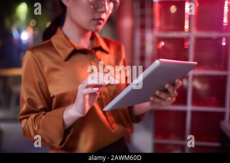 Cropped portrait of contemporary Asian businesswoman using digital tablet while working in futuristic office interior Stock Photo