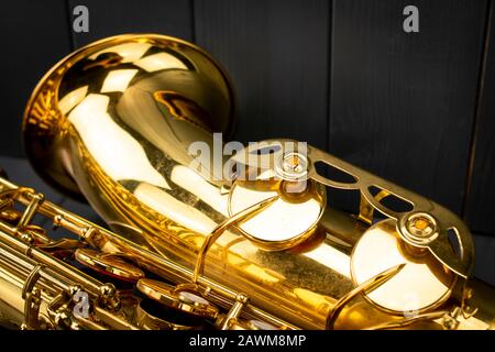 The bell and some notes keys of a tenor saxophone in the foreground on gray wooden background