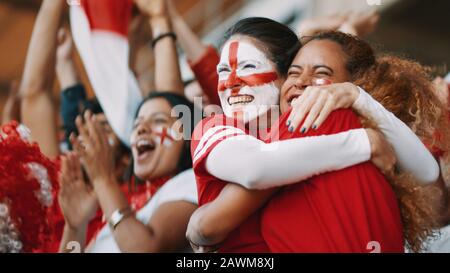 English female soccer fans with England flag painted on their faces hugging each other after their team's victory. English female spectators in footba Stock Photo