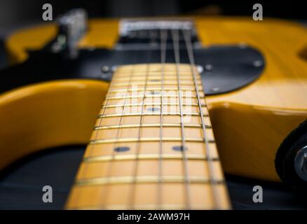 Close-up of the mast, frets and strings of a classic electric guitar, in yellow and black, bright on gray wood Stock Photo