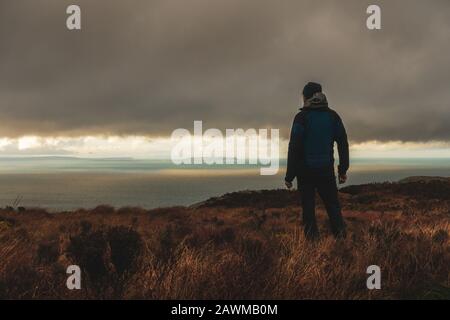 Person admiring the view from the Mull of Kintyre to Northern Ireland and Rathlin island in dramatic weather conditions in winter, Scotland, UK Stock Photo