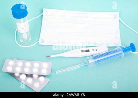 cold remedies. test tube, syringe, pills and medical mask respirator, thermometer on blue background. Stock Photo