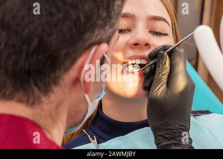 dentist examines the teeth of a girl patient with a mirror Stock Photo