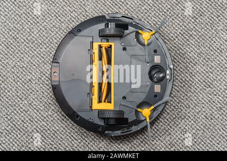 upside down robot vacuum cleaner lying on a carpet for cleaning brushes and a waste bin Stock Photo