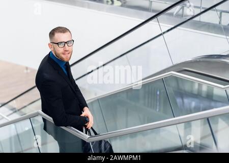 Elegant adult man standing on stairs with cellular in hand. He looking aside and smiling Stock Photo