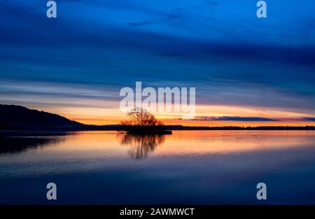 Winter sunrise at a calm loch with island and hillside. Loch Leven National Nature Reserve, Scotland, UK. Stock Photo