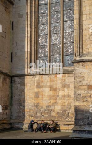The west tower of York Minster caught in a winter sun.  A group of three people shelter in the tower’s wing underneath a stained-glass window. Stock Photo