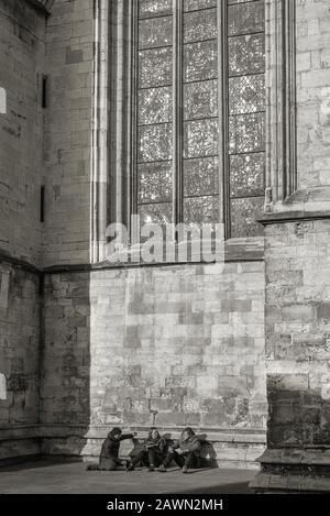 The west tower of York Minster caught in a winter sun.  A group of three people shelter in the tower’s wing underneath a stained-glass window. Stock Photo