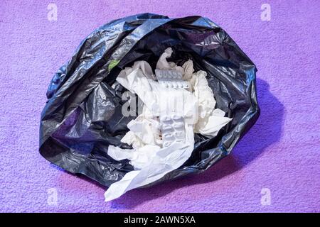A black plastic bin bag with screwed up used tissues and empty tablet blister packs Stock Photo