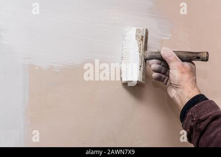 Master prime a putty wall before applying a decorative layer of plaster. Work process close-up. Interior repairs work. Stock Photo