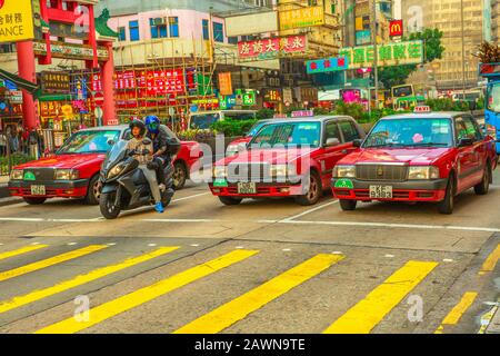 Hong Kong, China - December 5, 2016: red taxi cars in Jordan road and Shanghai street crossroad, at twilight. Temple Street gate on background. Stock Photo