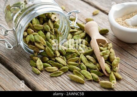 Green aromatic cardamom pods. Jar of whole cardamom pods and mortar of crushed seeds on table. Stock Photo