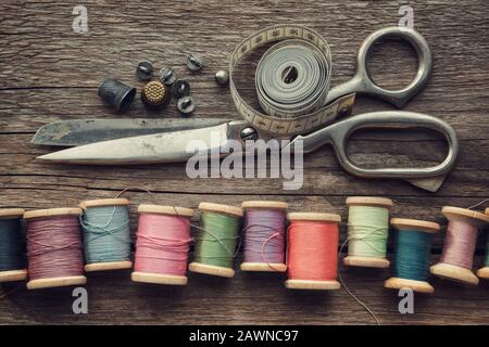 Row of vintage wooden spools of multicolored threads, tailoring scissors, thimbles, measuring tape, sewing items on wooden board. View from above. Stock Photo