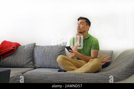 Man sitting on a sofa behind a white wall thinking about something Stock Photo