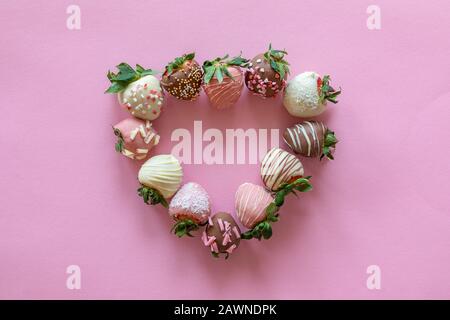 Heart shaped from handmade chocolate covered strawberries with different toppings on pink background Stock Photo