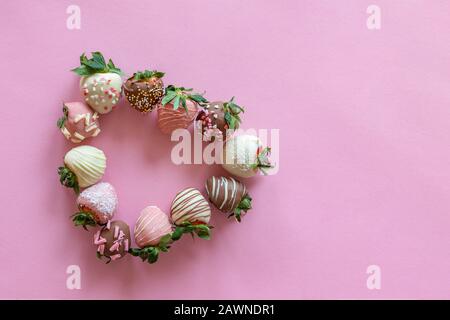 Heart shaped from handmade chocolate covered strawberries with different toppings on pink background Stock Photo