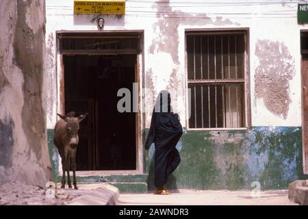 Muslim woman walking by shop in old town of Lamu, Indian Ocean coast of Kenya. Lamu was on major trading route centuries ago from Arabia to Zanzibar on coast of East Africa. Stock Photo