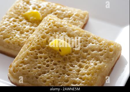 Hot toasted fresh square crumpets with dollops of melting butter served on a square plate for morning breakfast Stock Photo