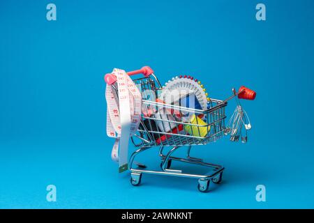 sewing accessories in the grocery basket, needles, threads, scissors, thimble on a blue background back Stock Photo
