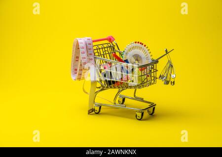 sewing accessories in the grocery basket, needles, threads, scissors, thimble on a yellow background Stock Photo